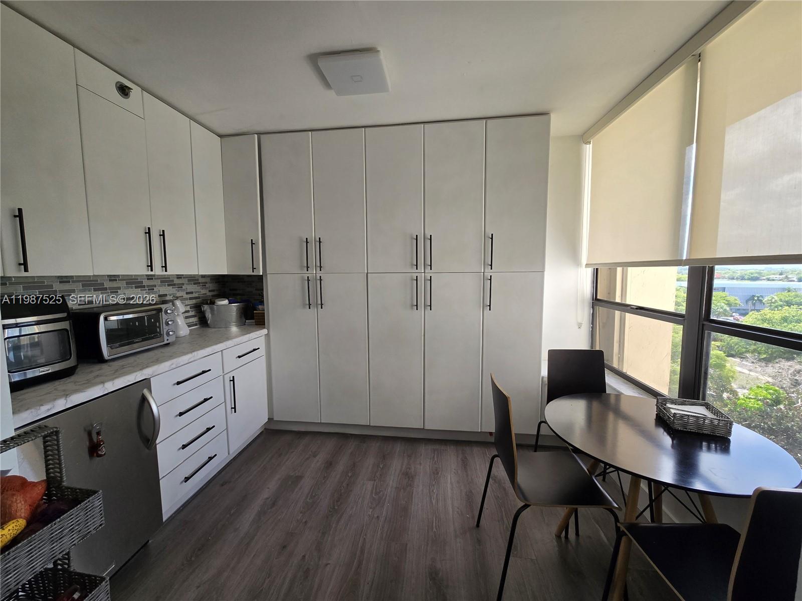 A kitchen features white cabinetry, a marble-look countertop, dark wood flooring, and a dining area — 900 NE 195th St # 709, Miami FL 33179, MIAMI, FL