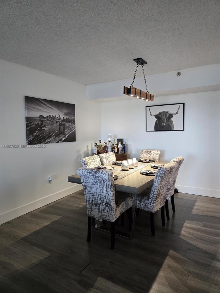A dining room features a wooden table, patterned chairs, a linear pendant light, and wall art — 900 NE 195th St # 709, Miami FL 33179, MIAMI, FL
