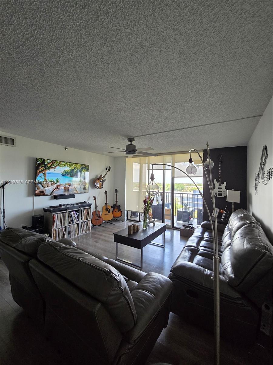 A living room features leather sofas, a television, musical instruments, and a balcony view — 900 NE 195th St # 709, Miami FL 33179, MIAMI, FL