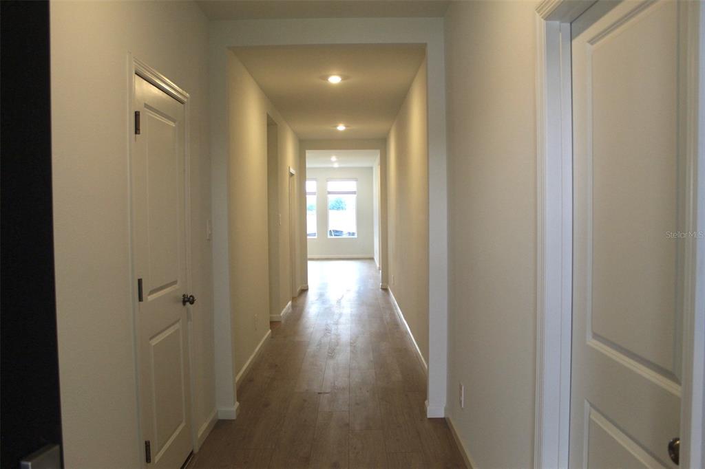 A long hallway with light wood-look flooring leads toward a bright room with windows — 4359 VIBERNUM AVENUE, ST CLOUD, FL