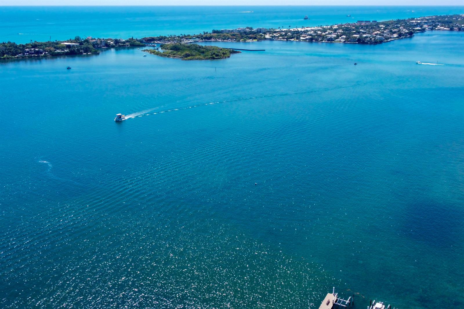 An aerial view of a boat traveling across a large, blue bay near coastal homes — 8200 Lakeshore Drive # 202, Hypoluxo FL 33462, HYPOLUXO, FL