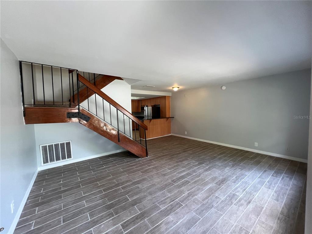 An open-concept living room features wood-look tile flooring and a wooden staircase with black railings — 14627 PINE GLEN CIRCLE, LUTZ, FL