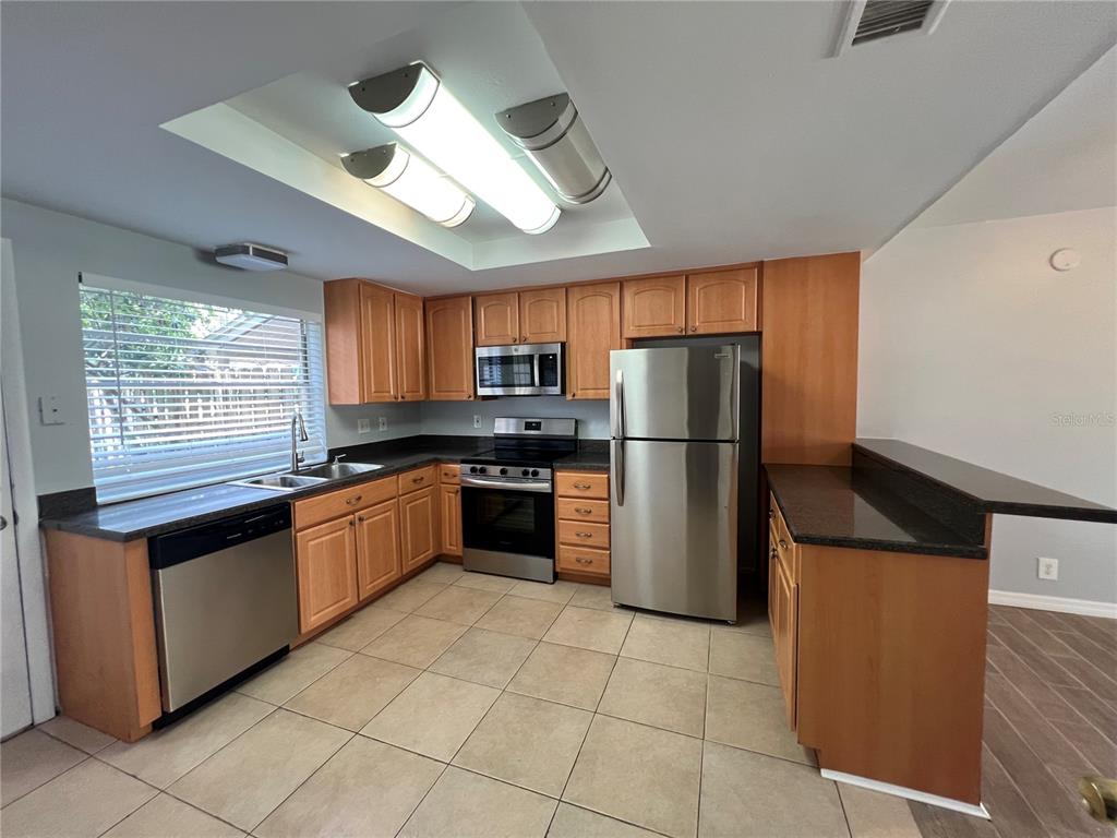 A kitchen features light wood cabinets, stainless steel appliances, dark countertops, and tile flooring — 14627 PINE GLEN CIRCLE, LUTZ, FL