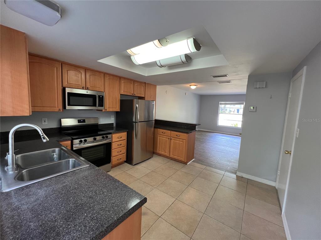 A kitchen with wood cabinets, stainless steel appliances, and dark countertops opens to a living area — 14627 PINE GLEN CIRCLE, LUTZ, FL
