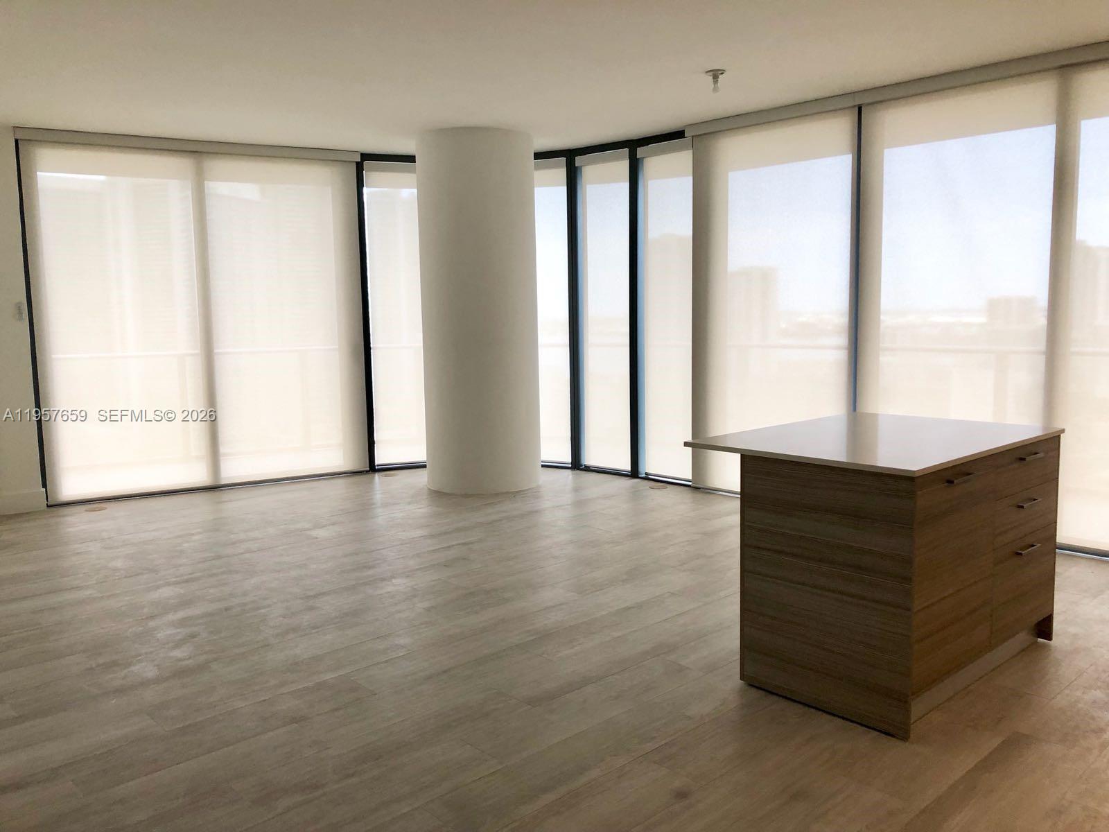 An empty room features light wood-look flooring, a central structural column, and floor-to-ceiling windows — 121 NE 34th St # 2704, Miami FL 33137, MIAMI, FL