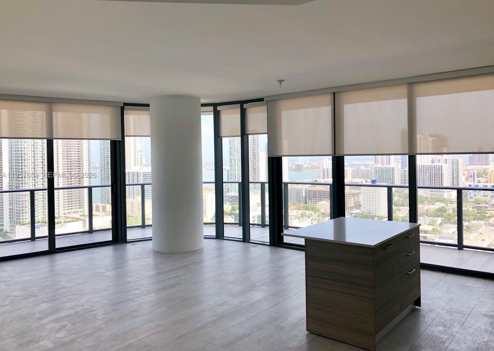 An empty room with light wood floors, a central pillar, and floor-to-ceiling windows overlooking a city — 121 NE 34th St # 2704, Miami FL 33137, MIAMI, FL