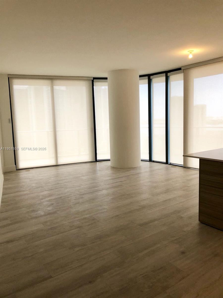 An empty room features light wood-look flooring, a central structural column, and floor-to-ceiling windows — 121 NE 34th St # 2704, Miami FL 33137, MIAMI, FL