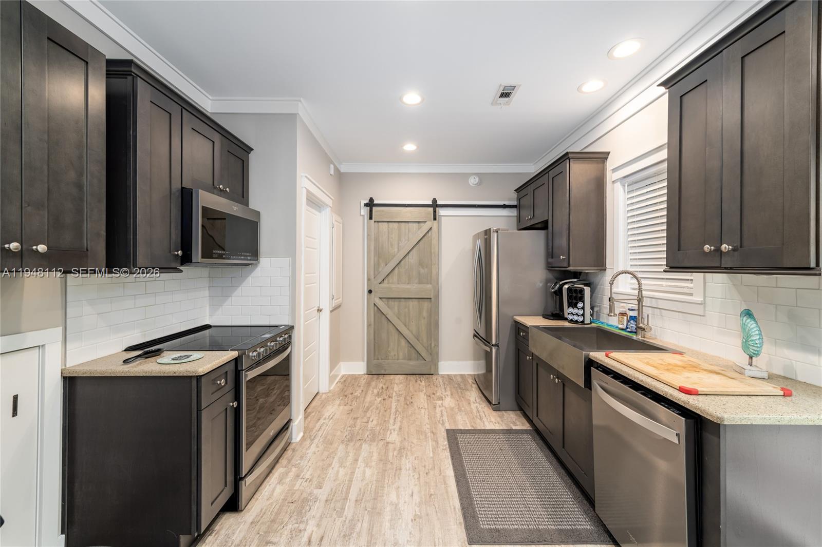 A galley kitchen features dark cabinets, stainless steel appliances, a farmhouse sink, and barn door — 101 11th Street Ocean, Unit 17, Marathon FL 33050, MARATHON, FL