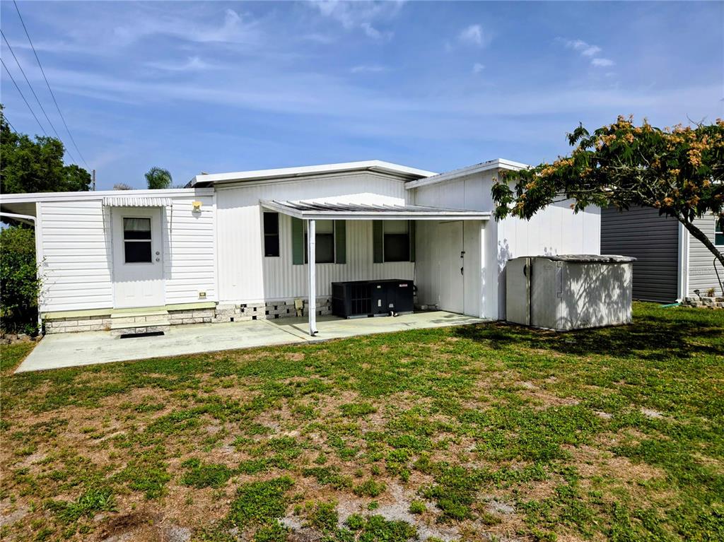 The exterior of a white mobile home features a covered concrete patio and an air conditioner — 6253 BALMY LANE, ZEPHYRHILLS, FL