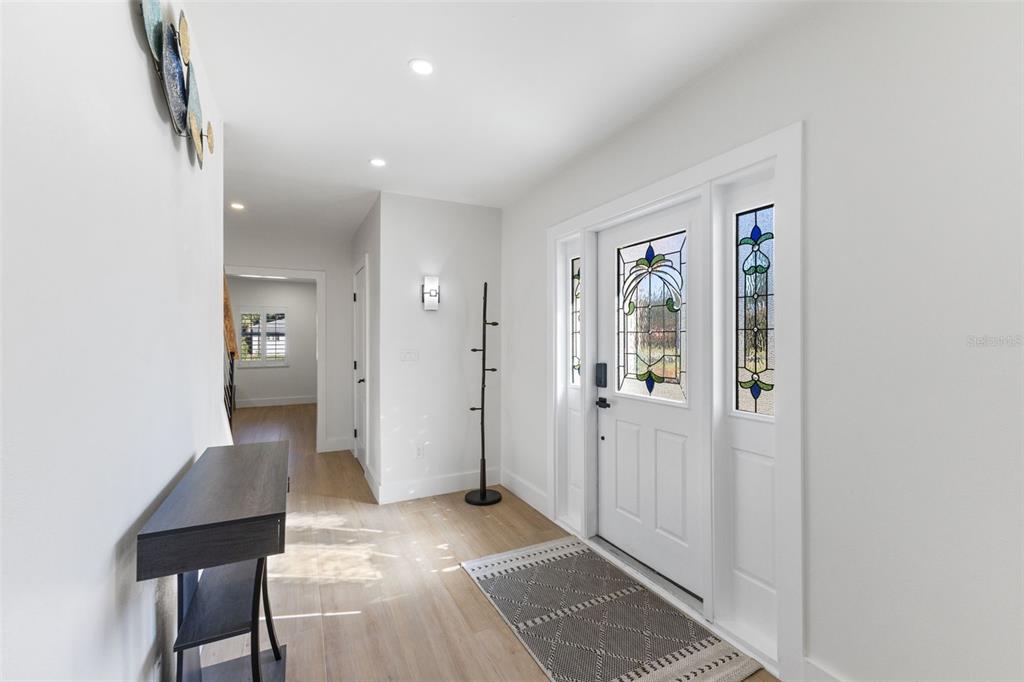 A bright entryway features light wood flooring, a white front door with stained glass, and decor — 7100 PARK STREET S, ST PETERSBURG, FL