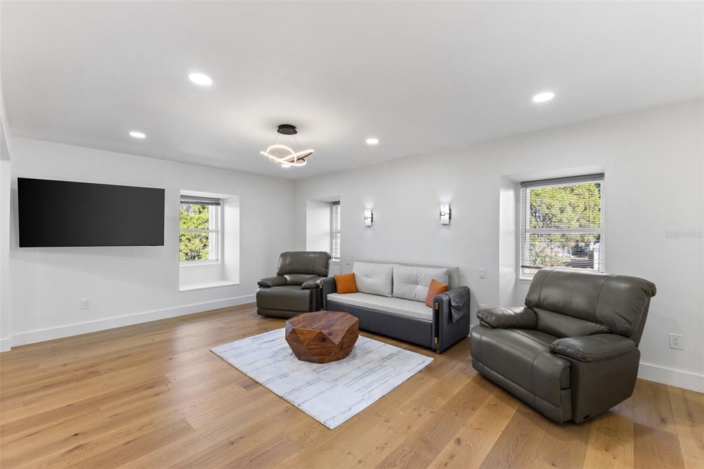 A living room features light wood floors, a gray sofa, two recliners, and a television — 7100 PARK STREET S, ST PETERSBURG, FL