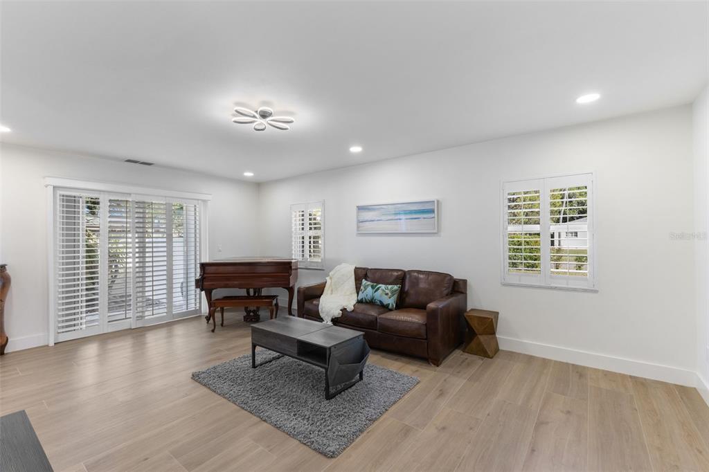 A living room features light wood-look flooring, a brown leather sofa, and a grand piano — 7100 PARK STREET S, ST PETERSBURG, FL