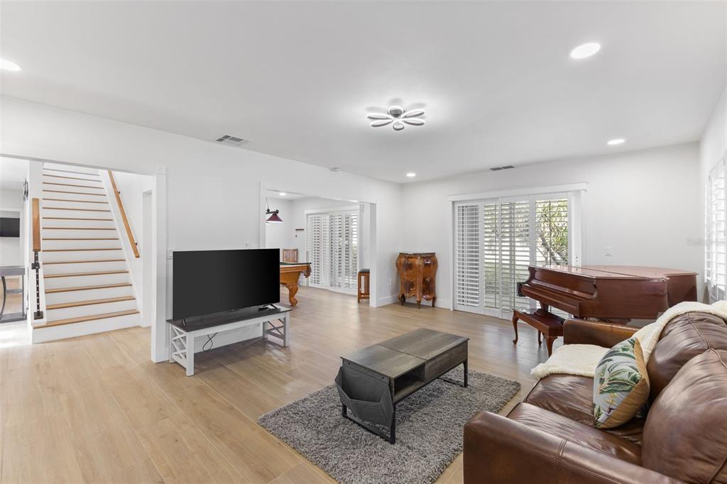 A living room features light wood floors, a brown leather sofa, a piano, and stairs — 7100 PARK STREET S, ST PETERSBURG, FL