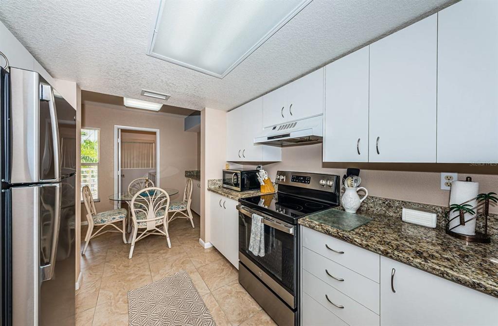 A kitchen with white cabinets, granite countertops, stainless steel appliances, and an adjacent dining area — 6093 BAHIA DEL MAR CIRCLE UNIT 478, ST PETERSBURG, FL