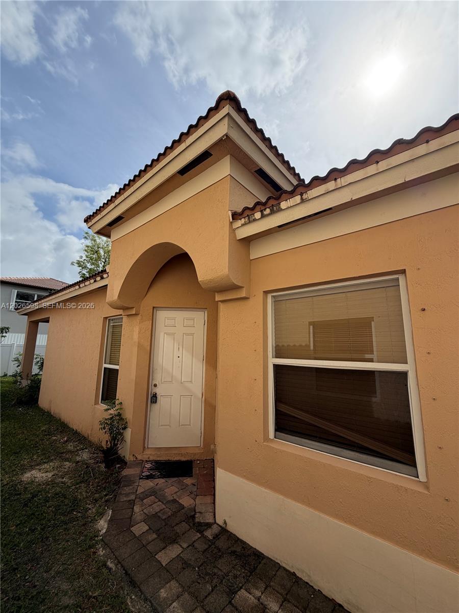 The exterior of a peach-colored house features a white front door and a tiled walkway — 3951 NE 11th Dr, Homestead FL 33033, HOMESTEAD, FL