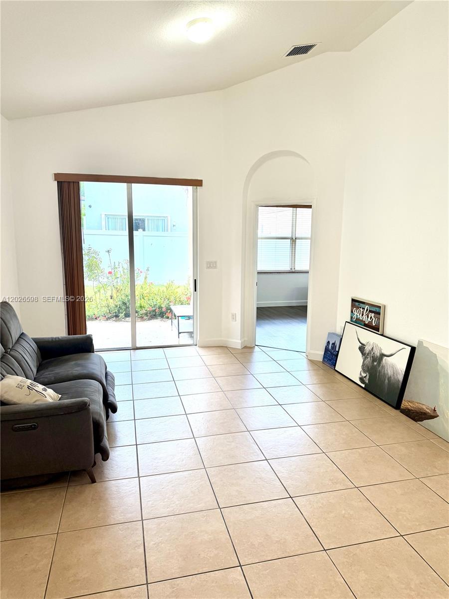 A living room features tile flooring, a gray sofa, and a sliding glass door — 3951 NE 11th Dr, Homestead FL 33033, HOMESTEAD, FL