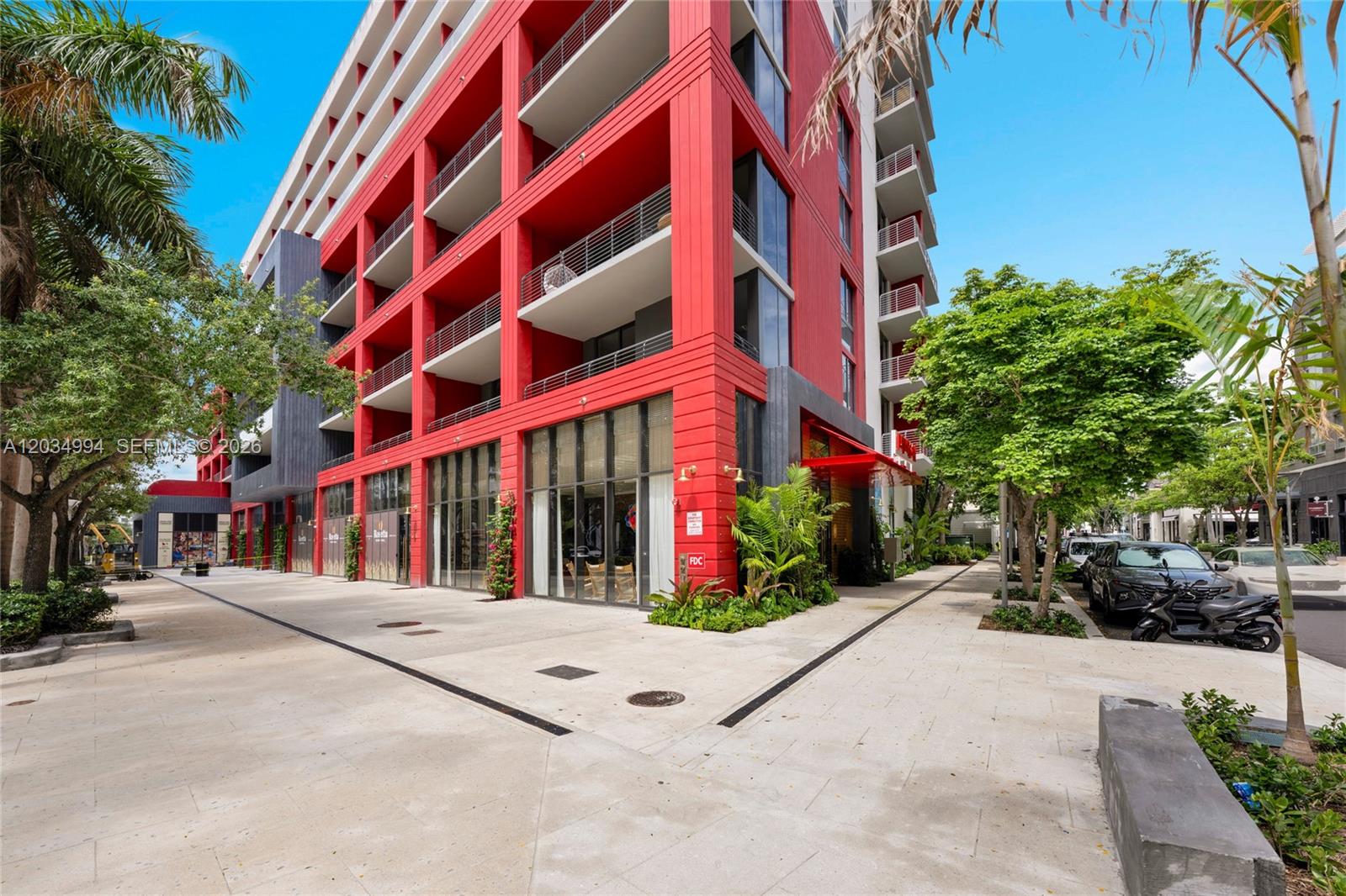A modern multi-story building features a vibrant red exterior with balconies and ground-level storefronts — 90 NE 32nd # 406, Miami FL 33127, MIAMI, FL