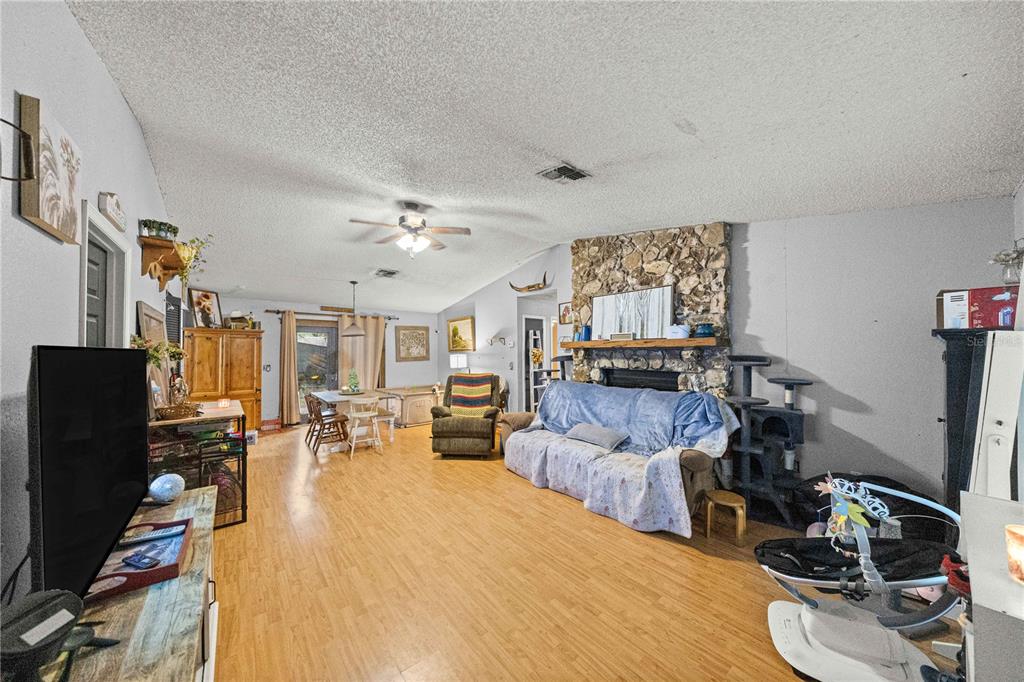 A living room features light wood flooring, a stone fireplace, and a ceiling fan — 3301 NE 23RD AVENUE, OCALA, FL
