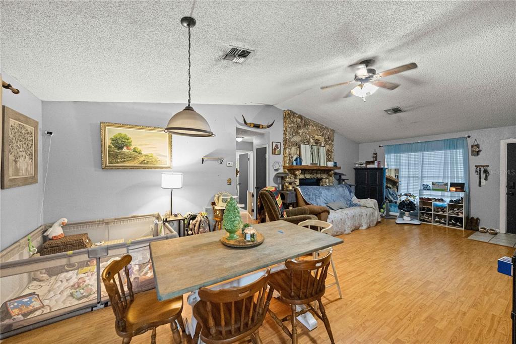 A dining area with a wooden table and chairs opens into a living room with stone fireplace — 3301 NE 23RD AVENUE, OCALA, FL