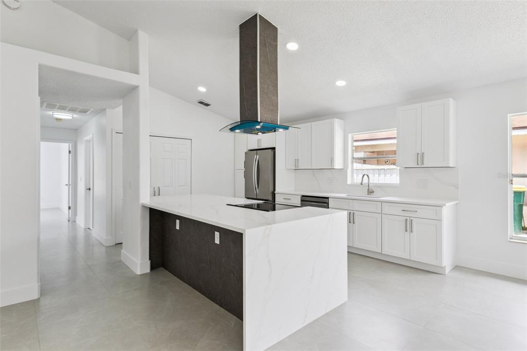 A modern kitchen features white cabinets, a marble-topped island, and a dark range hood — 2625 WALDEN COURT, KISSIMMEE, FL
