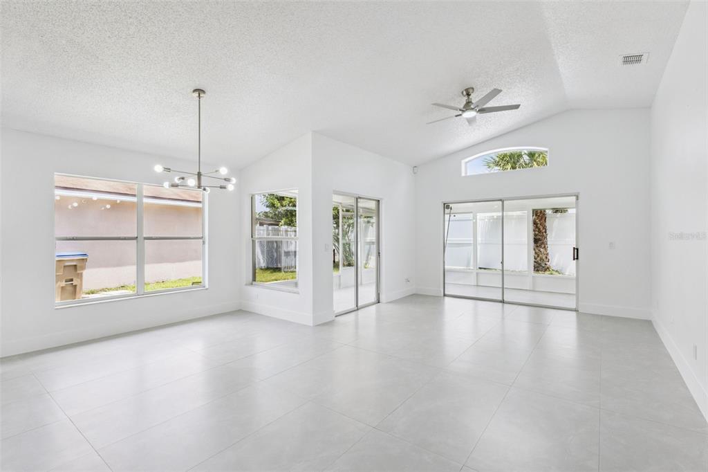 A bright, open-concept living and dining area features white walls, tile flooring, and vaulted ceilings — 2625 WALDEN COURT, KISSIMMEE, FL