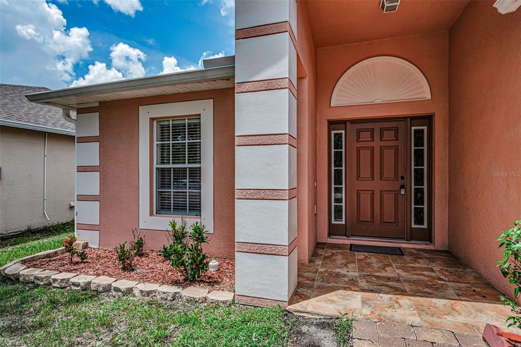 The exterior of a house features a brown front door, a window, and tiled flooring — 17029 TORVEST COURT, LAND O LAKES, FL