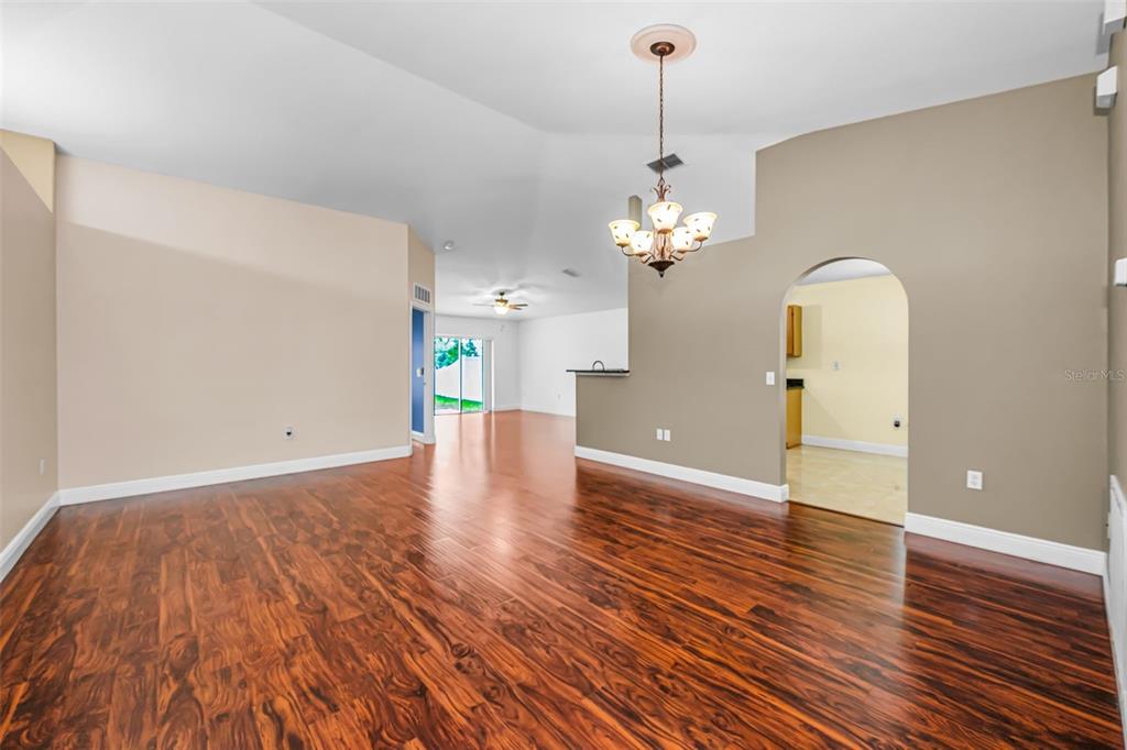 An empty living room features dark hardwood floors, a vaulted ceiling, and a dining chandelier — 17029 TORVEST COURT, LAND O LAKES, FL