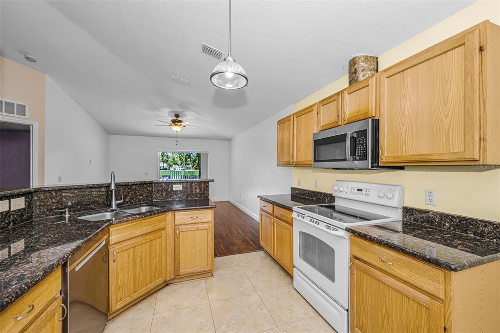 A kitchen features light wood cabinets, dark granite countertops, white appliances, and tile flooring — 17029 TORVEST COURT, LAND O LAKES, FL