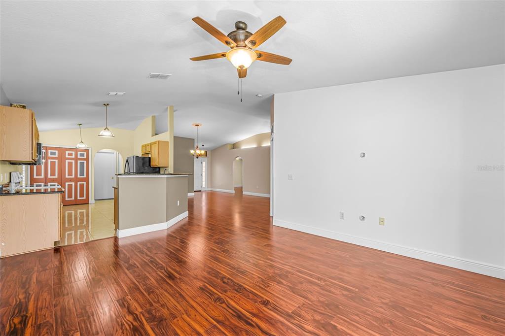 An open-concept living area features wood-look flooring, a ceiling fan, and an adjacent kitchen — 17029 TORVEST COURT, LAND O LAKES, FL
