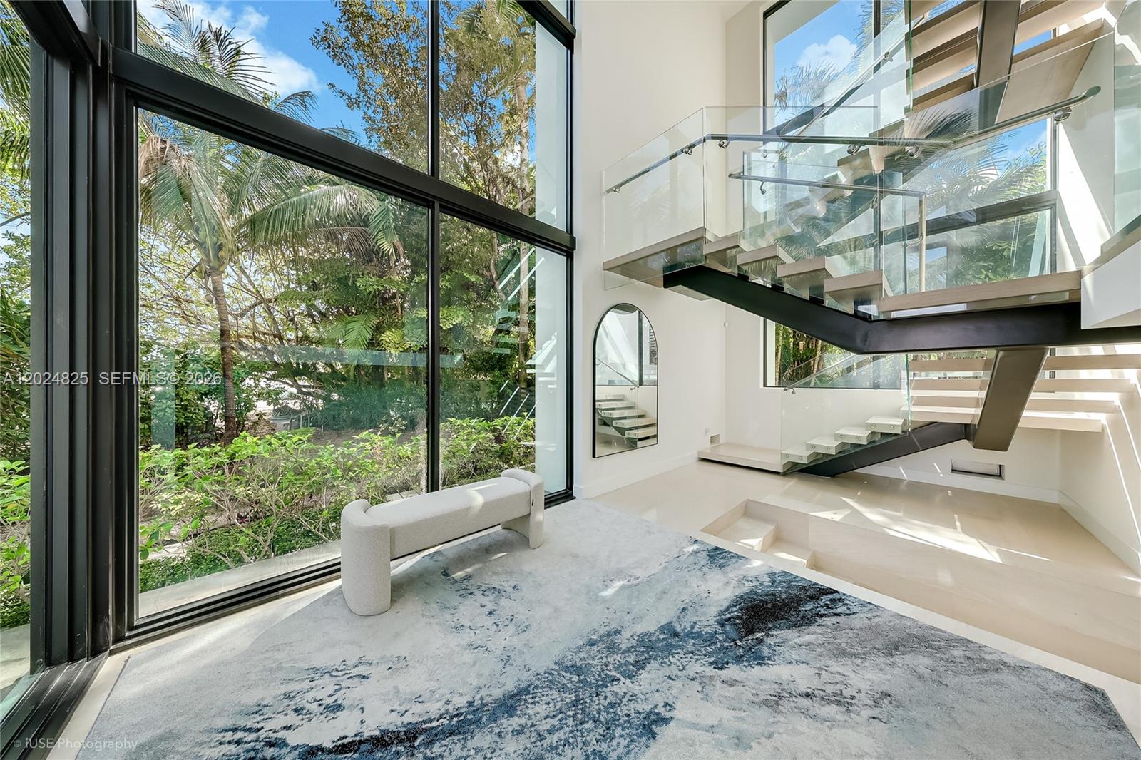A modern living room features a floating staircase, floor-to-ceiling windows, and a patterned area rug — 420 N Hibiscus Dr, Miami Beach FL 33139, MIAMI BEACH, FL
