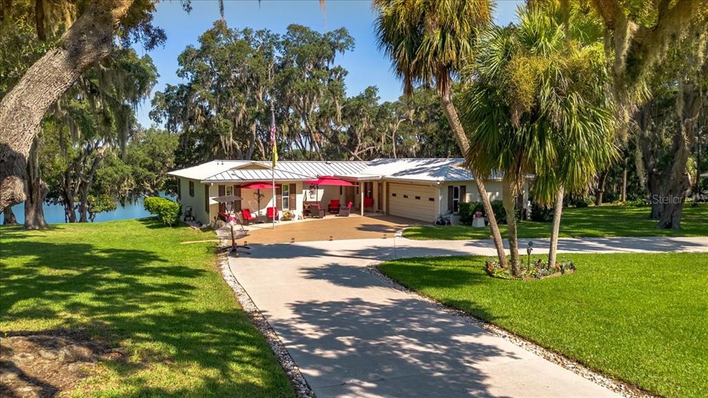 A single-story house with a metal roof and a concrete driveway sits near a lake — 10522 SE 146TH TERRACE ROAD, OCKLAWAHA, FL