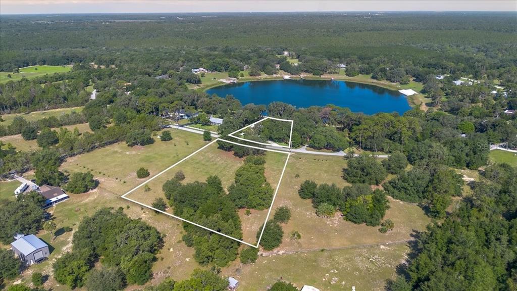 An aerial view shows a large, grassy lot outlined in white near a lake — 10522 SE 146TH TERRACE ROAD, OCKLAWAHA, FL