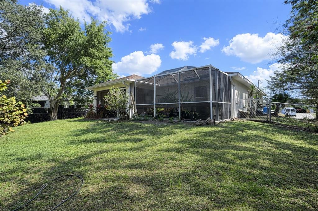 A backyard view of a house with a screened-in patio and a grassy lawn — 720 BRANNEN AVENUE, LEHIGH ACRES, FL
