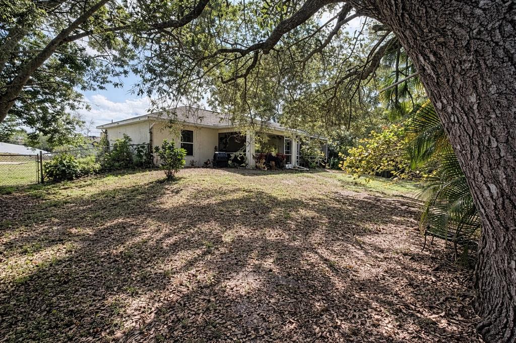 A backyard view of a single-story house with a screened porch and large oak trees — 720 BRANNEN AVENUE, LEHIGH ACRES, FL