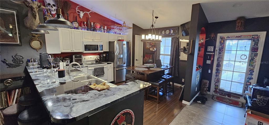 A kitchen and dining area features dark walls, white cabinets, and a marbled countertop island — 720 BRANNEN AVENUE, LEHIGH ACRES, FL