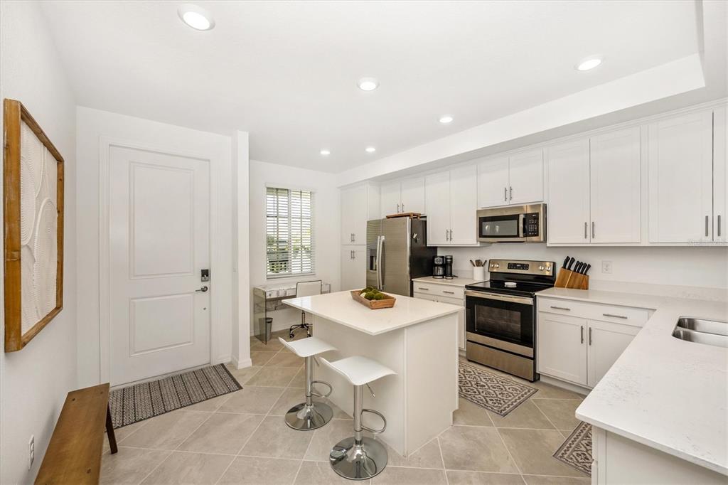 A modern kitchen features white cabinetry, stainless steel appliances, a central island, and tile flooring — 12240 WELLEN GOLF STREET UNIT 204, VENICE, FL