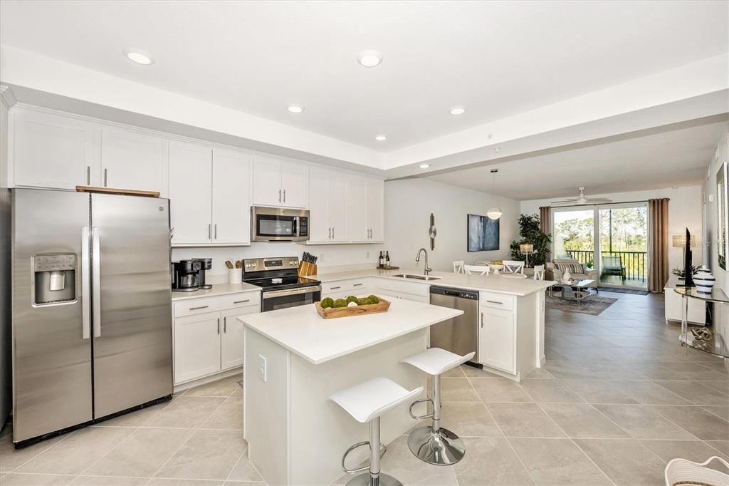 A modern kitchen with white cabinets, stainless steel appliances, and a central island with stools — 12240 WELLEN GOLF STREET UNIT 204, VENICE, FL