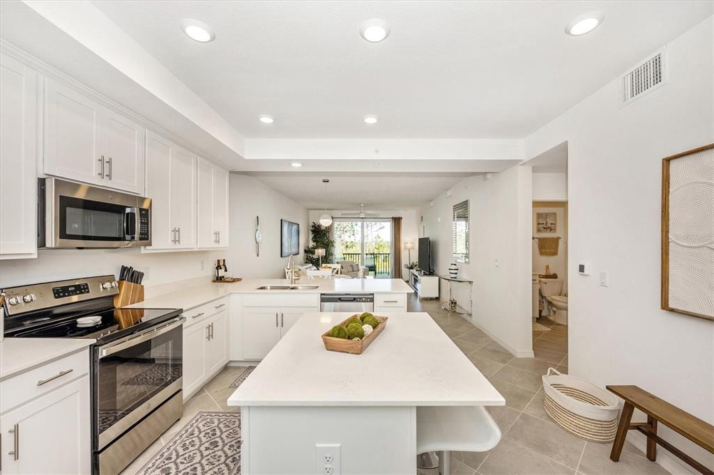 A white kitchen features a central island, stainless steel appliances, and tile flooring — 12240 WELLEN GOLF STREET UNIT 204, VENICE, FL