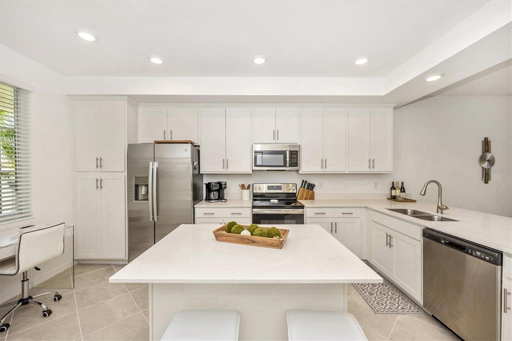 A modern kitchen features white cabinetry, stainless steel appliances, and a central island with seating — 12240 WELLEN GOLF STREET UNIT 204, VENICE, FL