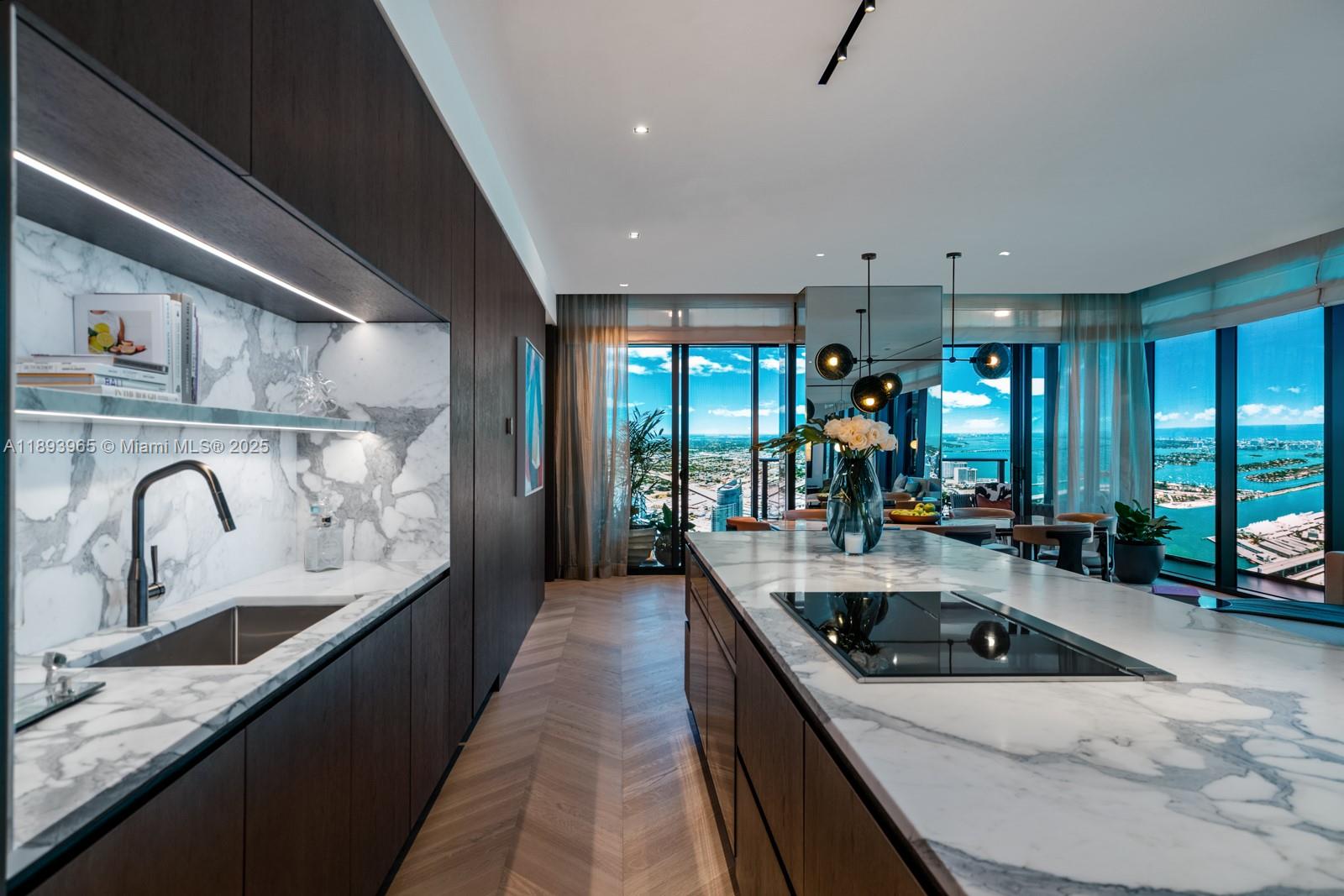 A modern kitchen features dark wood cabinetry, marble countertops, and floor-to-ceiling windows with water views — 300 N Biscayne Blvd # 7803, Miami FL 33132, MIAMI, FL