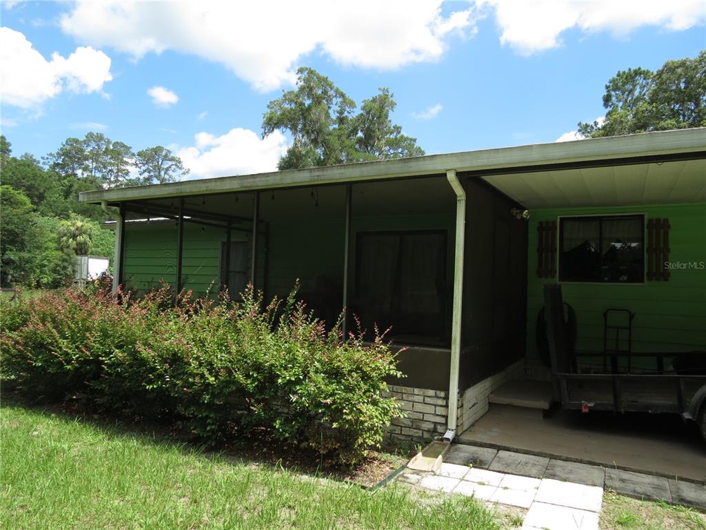 A green house features a screened-in porch, a carport, and a large hedge in front — 8545 S MAGNOLIA AVENUE, OCALA, FL