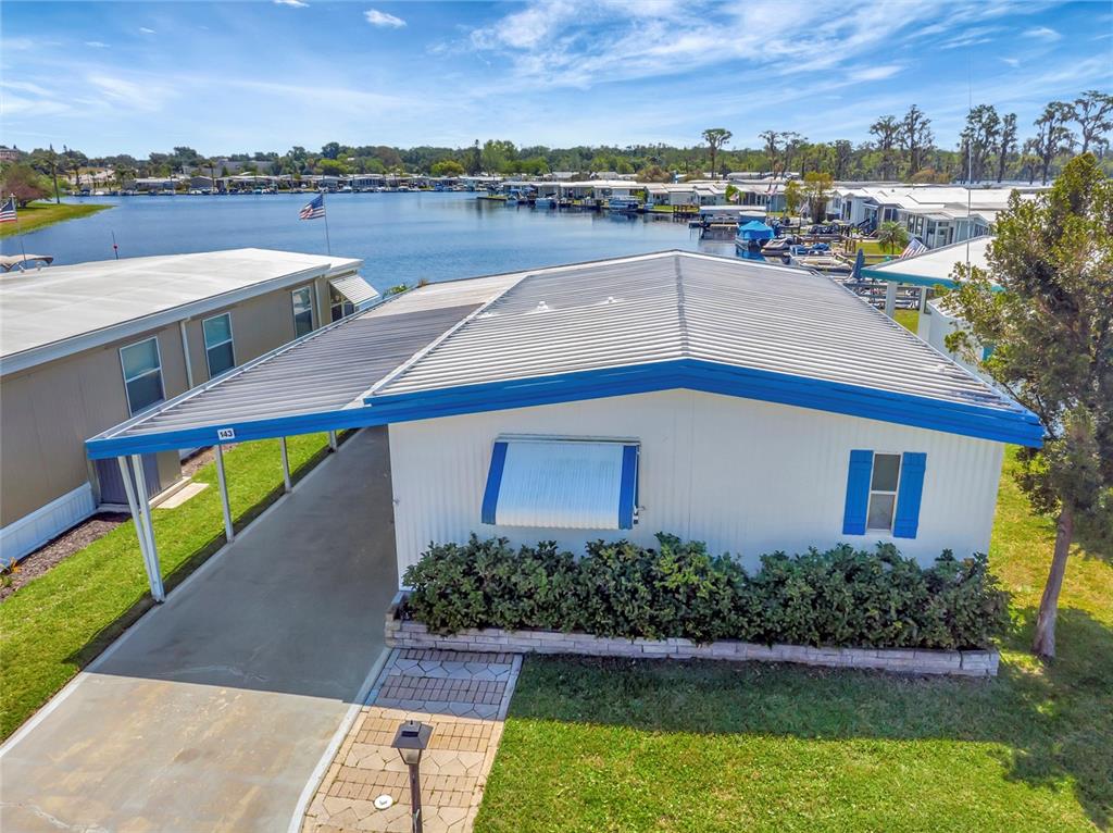An exterior view of a mobile home with a carport, blue trim, and waterfront access — 1401 W HIGHWAY 50 UNIT 143, CLERMONT, FL