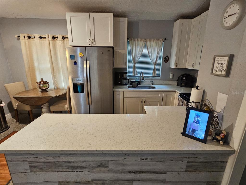 A kitchen features white cabinets, stainless steel appliances, a quartz countertop, and a small dining area — 730 SEMINOLA BOULEVARD, CASSELBERRY, FL