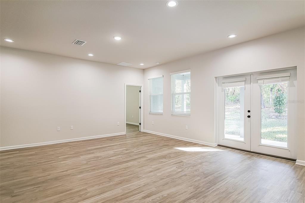 A bright, empty room features light wood-look flooring, recessed lighting, two windows, and glass doors — 20 GREENTREE STREET, HOMOSASSA, FL
