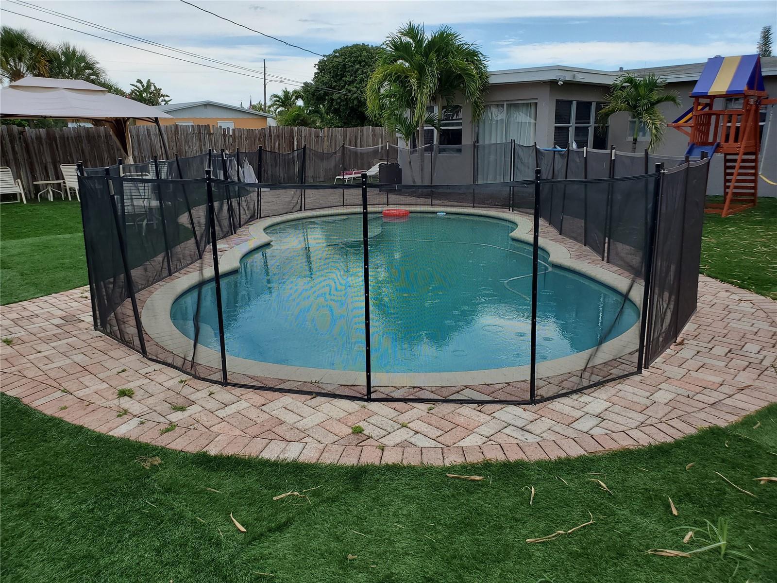 A backyard swimming pool is enclosed by a black mesh safety fence on a brick patio — 811 S Broadway, Lantana FL 33462, LANTANA, FL