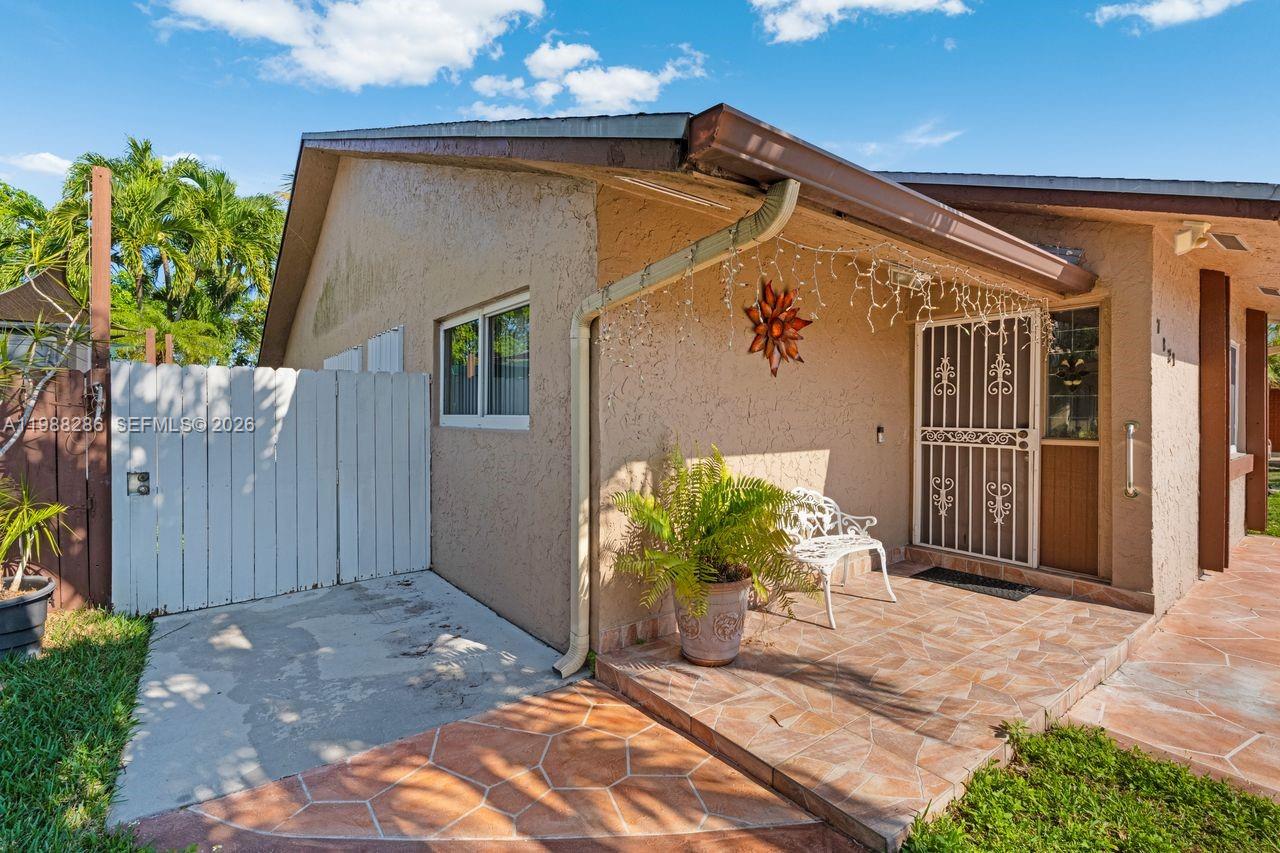 A tan stucco house exterior features a tiled patio, white fence, and decorative metal door — 7821 SW 148th Ave # 2, Miami FL 33193, MIAMI, FL