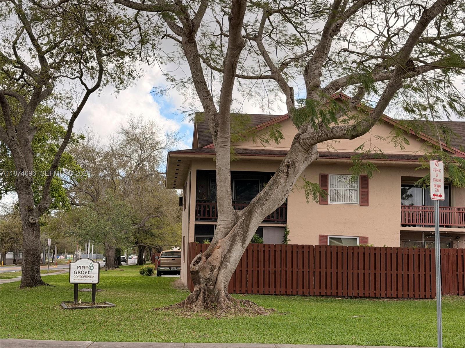 A multi-story tan condominium building stands behind a wooden fence and a large tree — 11295 SW 88th St # M109, Miami FL 33176, MIAMI, FL