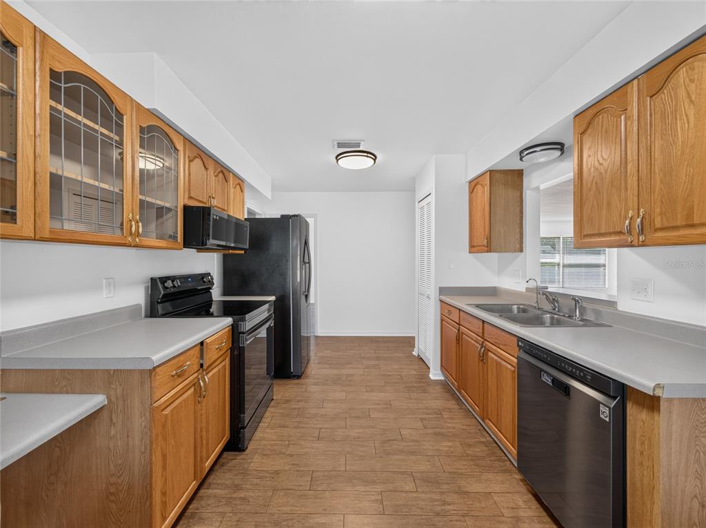 A kitchen features wood cabinets, black appliances, gray countertops, and wood-look tile flooring — 811 W HARBOUR COURT, OCOEE, FL