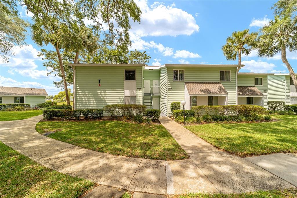 A two-story light green apartment building with a central staircase and surrounding landscaped lawn — 557 MIDWAY DRIVE UNIT B, OCALA, FL