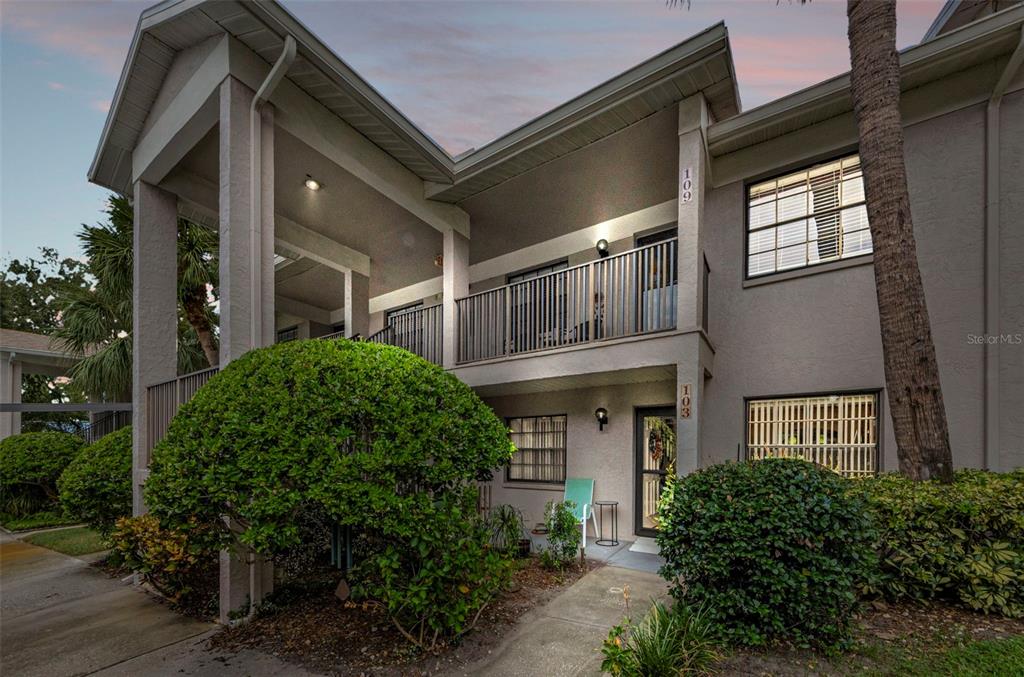 A two-story apartment building exterior features a ground-level entrance, a second-floor balcony, and landscaping — 2119 ELM STREET UNIT 103, DUNEDIN, FL